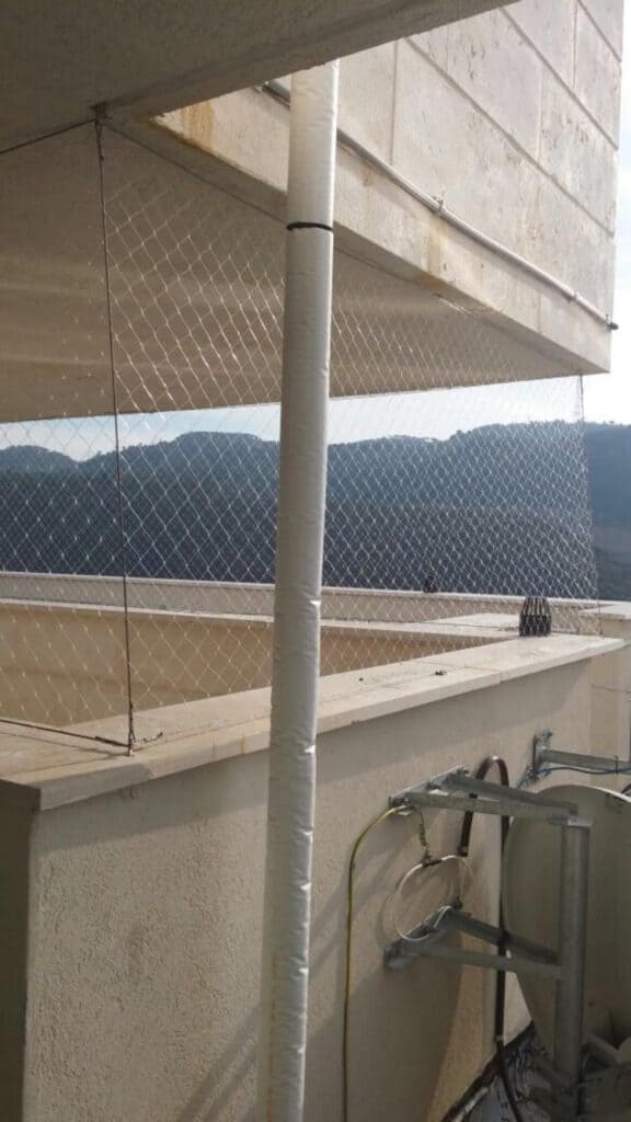 תיקון אינסטלציה בגובה — צינור חיצוני לאורך חזית בניין מגורים, צמוד למרפסת