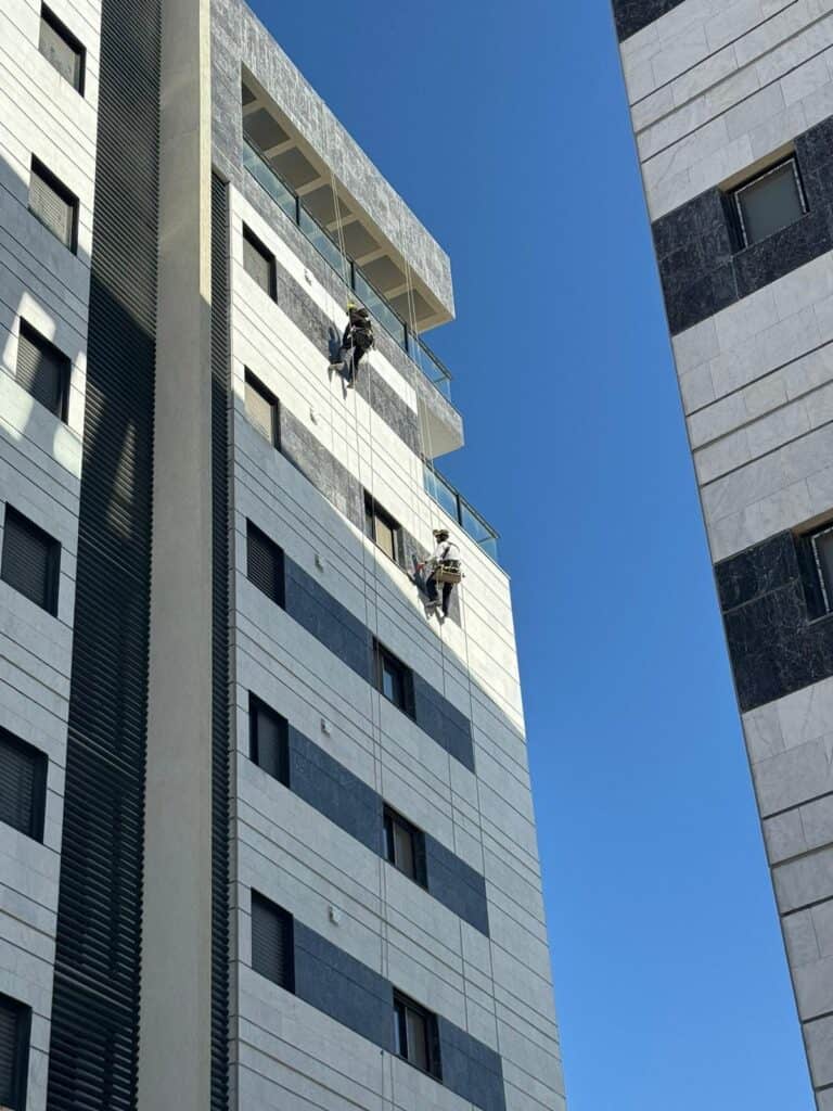 שני עובדים רתומים יורדים בסנפלינג מקצה גג מגדל לצורך טיפול בחזית