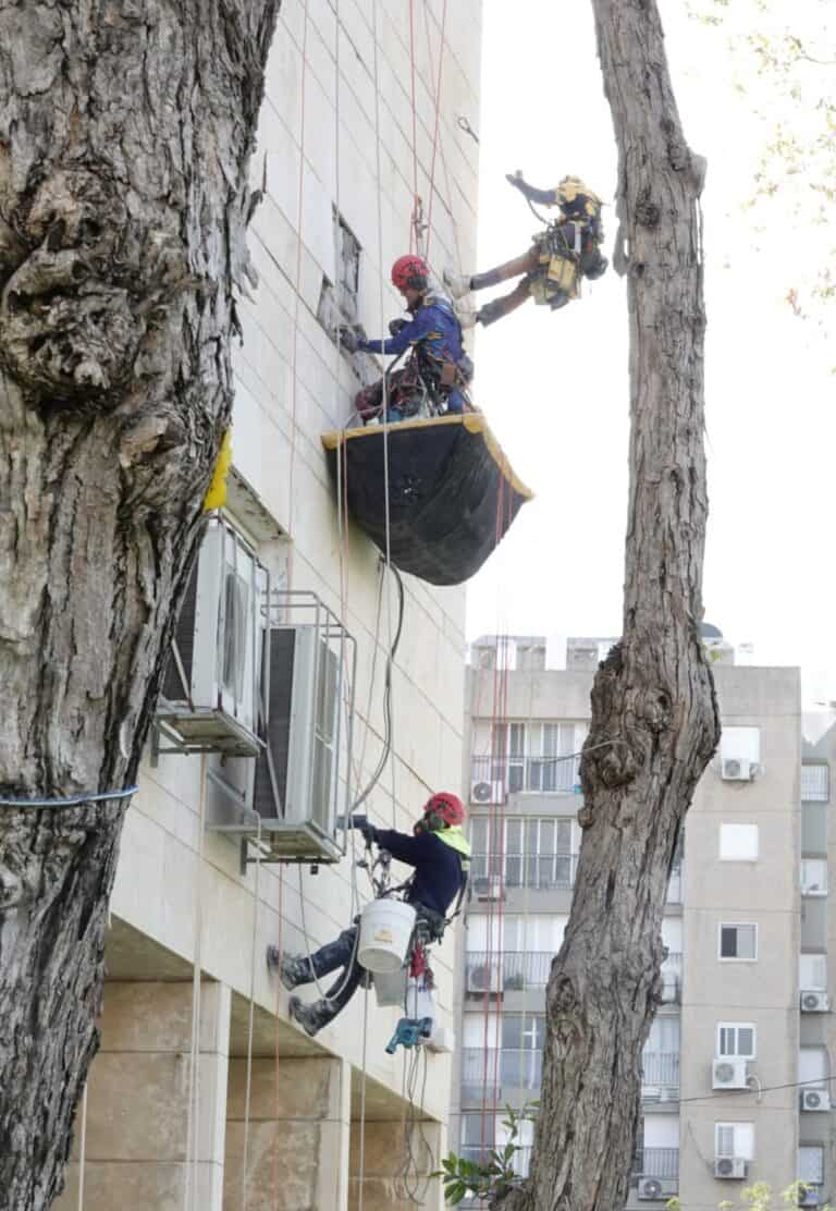 מאמרים עבודות בגובה – בסיס עבודות בגובה שלושה עובדים תלויים בחבלים סביב סל קליטה שחור בעת תיקון חיפוי בחזית בניין רב קומות