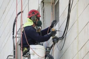 עובד בגובה מתקן ומחדש קיר חיצוני של בניין עם ציוד בטיחות מקצועי