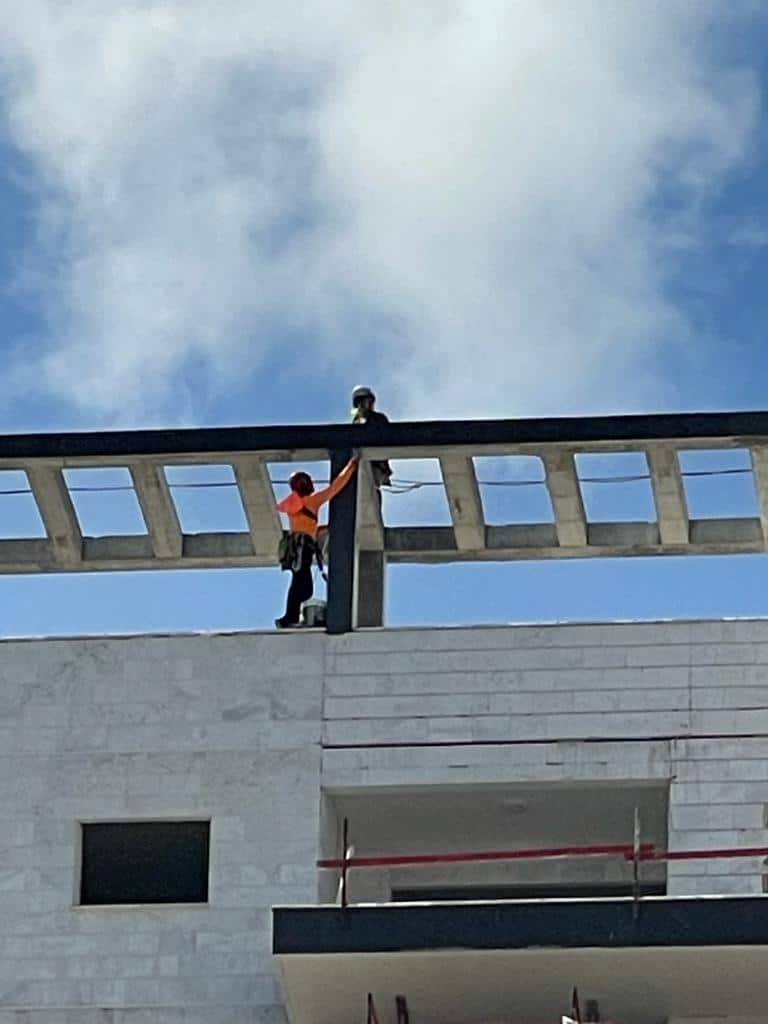 עובד רתום באפוד זוהר צועד על קורת בטון בראש שלד בניין חדש