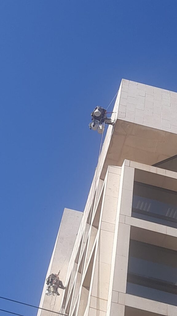 שני גולשי סנפלינג משתלשלים בחבלים מקצה גג של בניין מחופה אבן על רקע שמיים כחולים