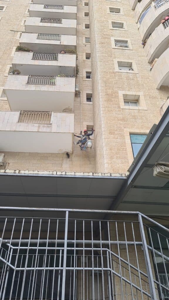 עובד תלוי בחבלים עם דלי ליד קיר בניין מגורים מחופה אבן מעל גגון הכניסה