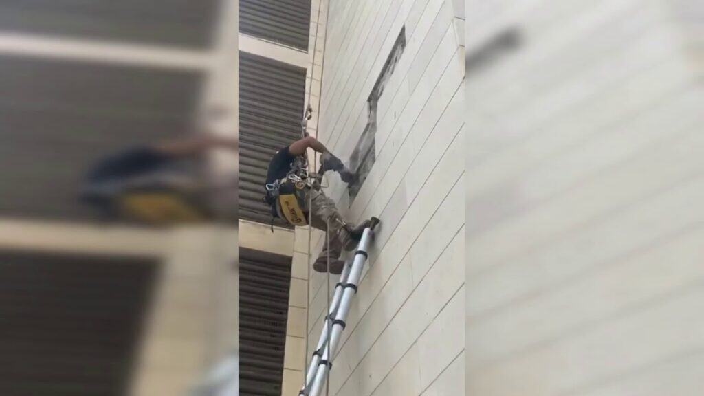 עובד בגובה על סולם, מבצע עבודות בנייה על קיר חיצוני של ב.