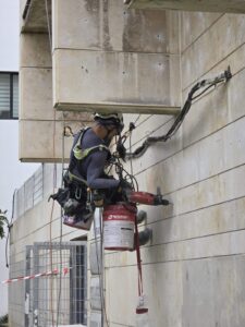 עובד בגובה עם ציוד בטיחות ומכשיר עבודה על קיר חיצוני של בניין.