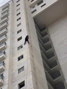 עובד בגובה מבצע עבודות בניין על קיר בניין גבוה.