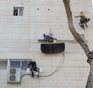 עובדי גובה מבצעים עבודות תחזוקה על קיר בניין גבוה.