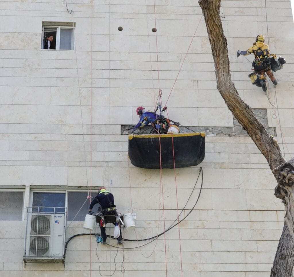 עובדי גובה מבצעים עבודות תחזוקה על קיר בניין גבוה.