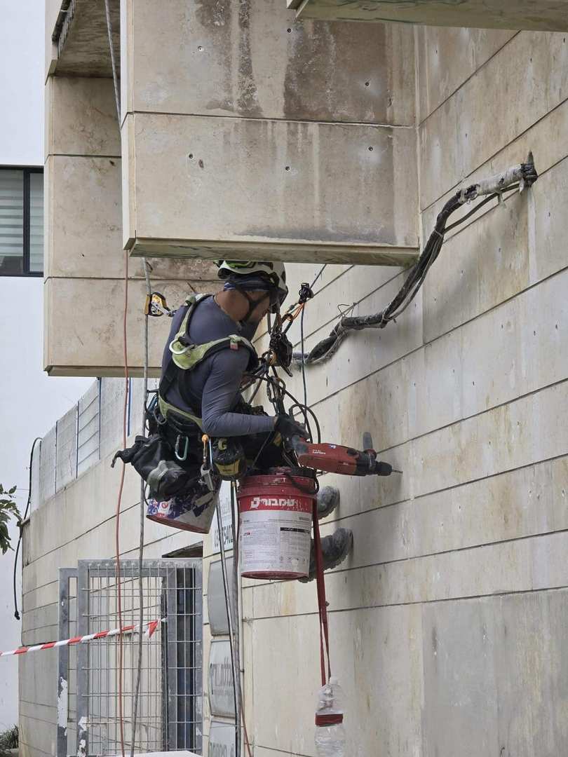 עבודות סנפלינג בגובה — עובד בגובה עם ציוד בטיחות ומכשיר עבודה על קיר חיצוני של בניין.