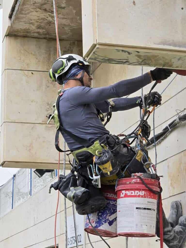 עובד בגובה עם ציוד בטיחות מבצע עבודות בניין.