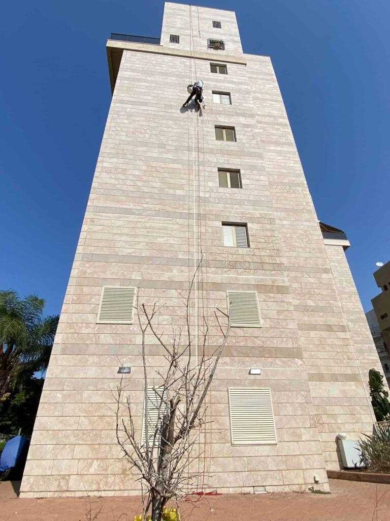 עובד בגובה מבצע עבודות בניין על קיר בניין גבוה.